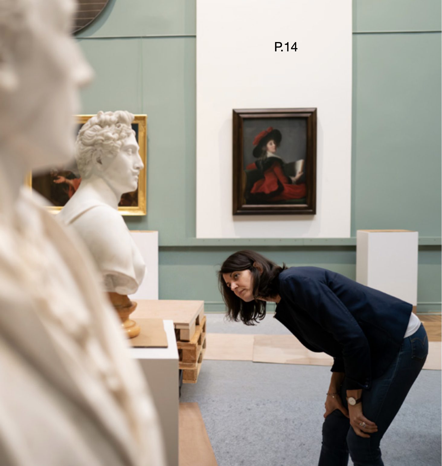 La même femme, penchée, observe de près un buste en marbre posé sur un socle, dans une galerie du musée.