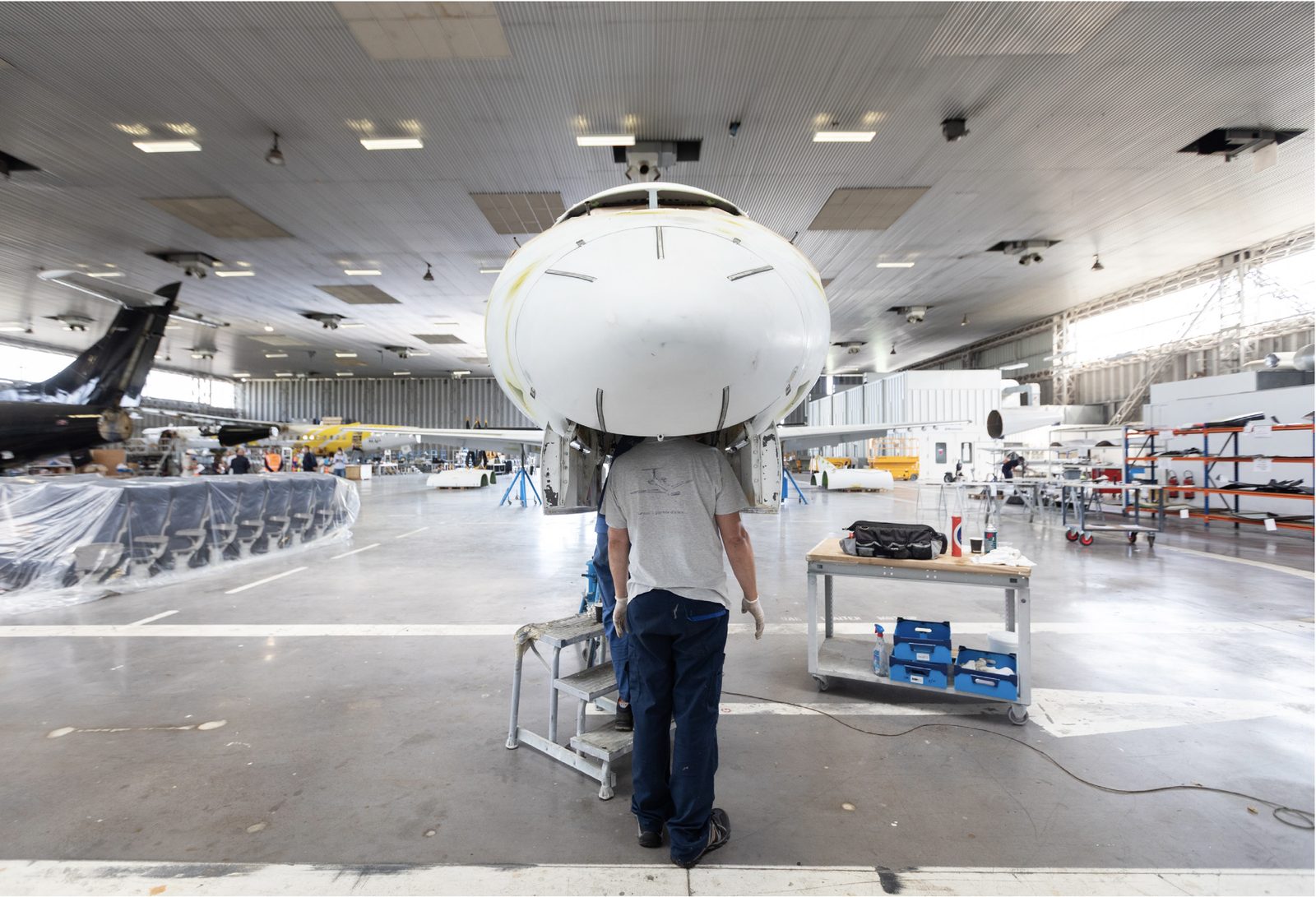 De dos, un technicien juché sur un escabeau observe le nez ouvert d'un Airbus A320 démonté, dans un hangar de Toulouse-Blagnac.