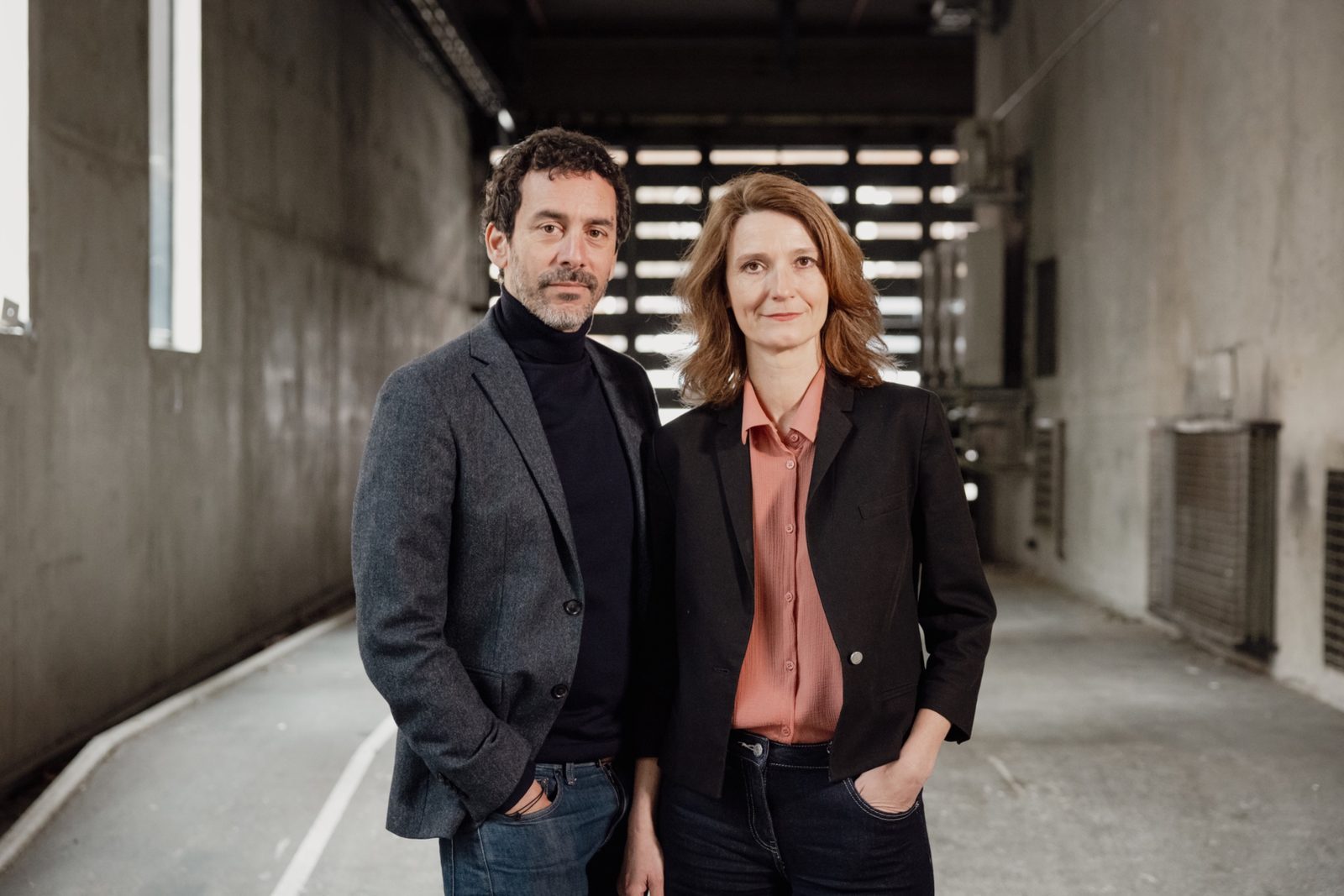Émilie Capliez et Matthieu Cruciani, debout côte à côte dans un couloir de béton.