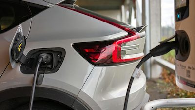 Gros plan sur l'arrière d'une voiture électrique blanche en charge, câble branché dans la trappe, sous un abri couvert.